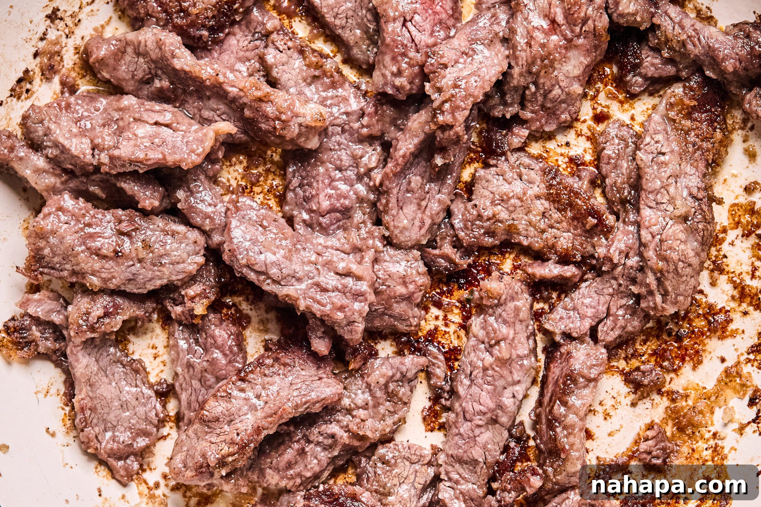 Half of the flank steak slices searing in a hot pan.