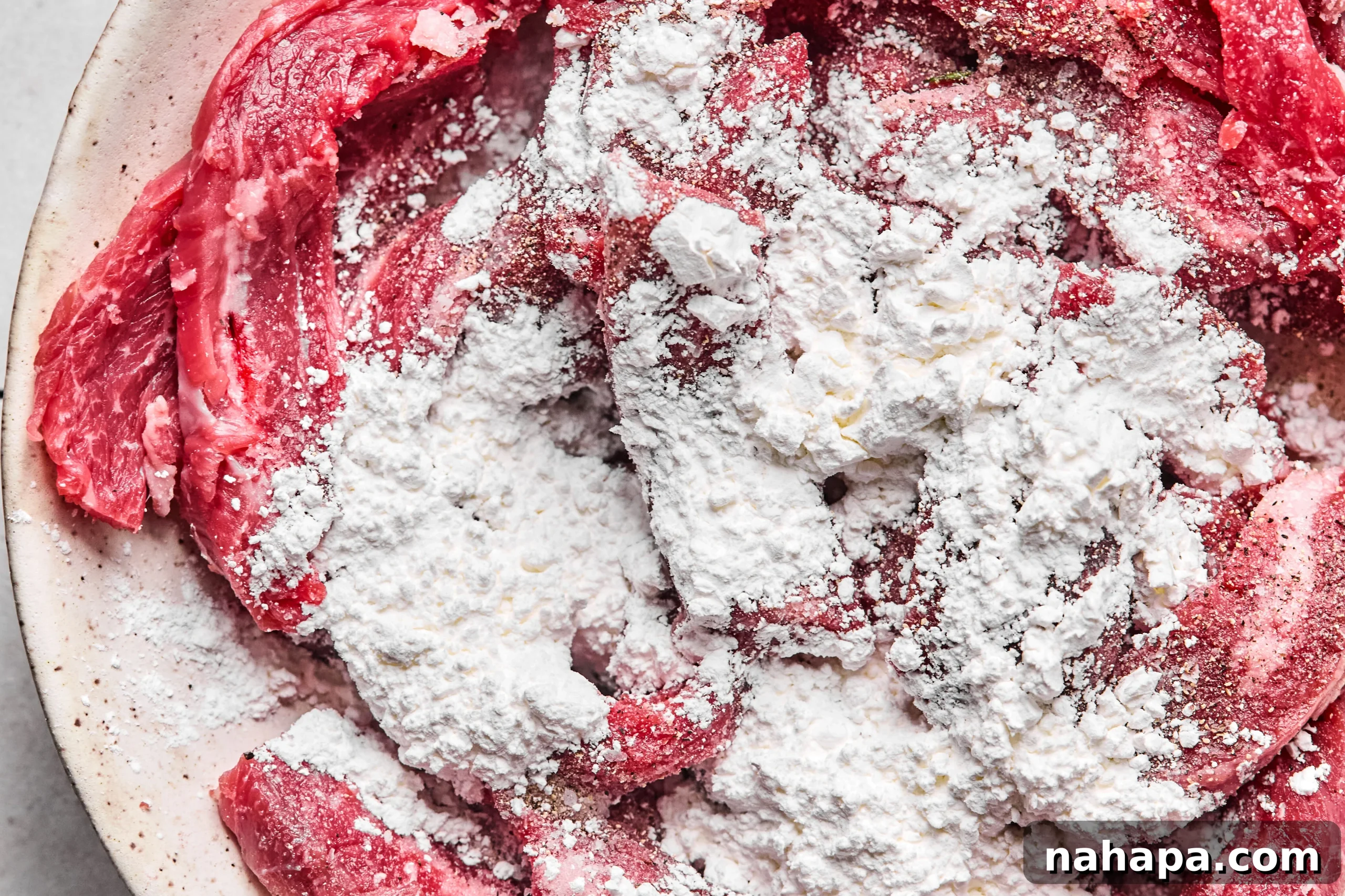 Sliced flank steak covered in salt, pepper, and arrowroot powder, ready for cooking.