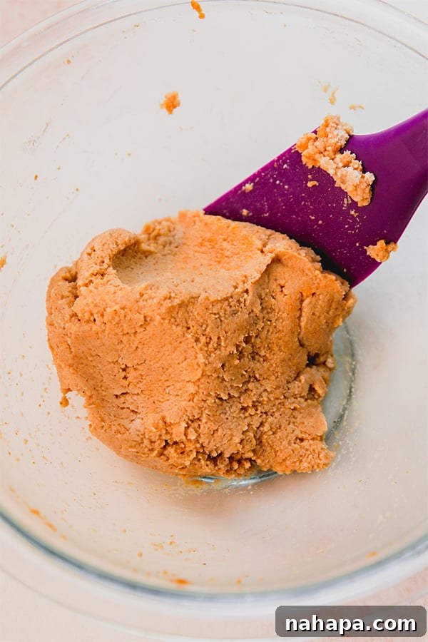 Fluffy Paleo Pumpkin Waffles Vegan Gluten Free 3 A bowl of thick, orange pumpkin waffle batter with a spoon resting inside, showing its rich texture.