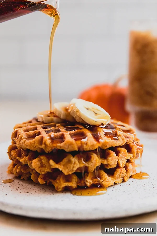 Fluffy Paleo Pumpkin Waffles Vegan Gluten Free 4 A stack of warm paleo and vegan pumpkin waffles adorned with banana slices and a rich pour of maple syrup, inviting a delightful breakfast.
