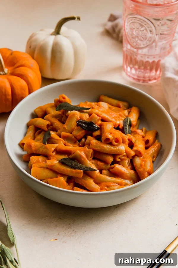 A beautifully plated bowl of gluten-free and dairy-free pumpkin penne alla vodka, garnished with fresh sage leaves.