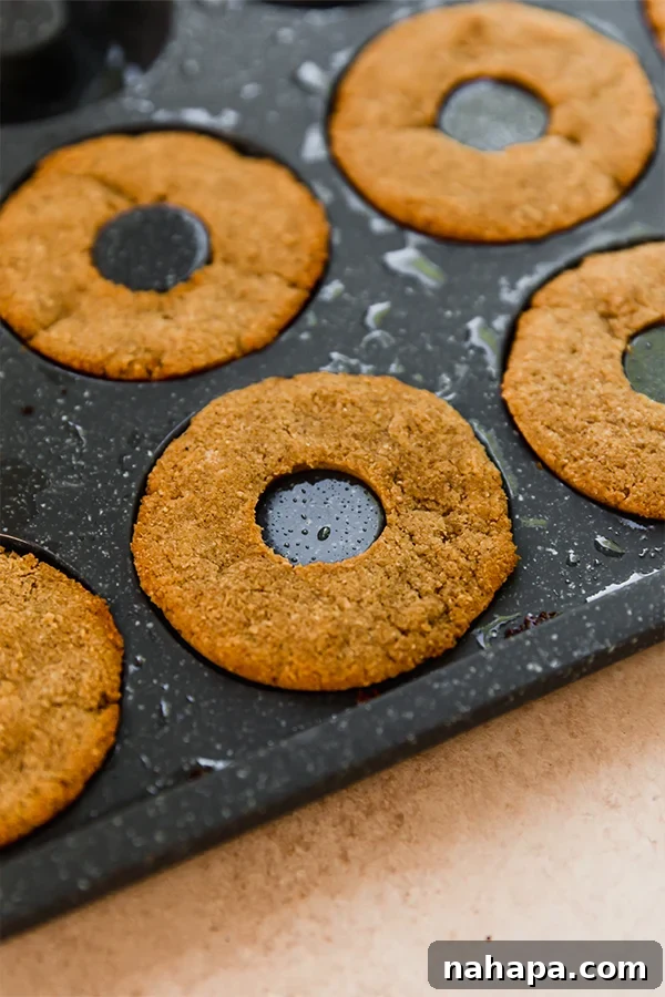 Mini apple cider donuts baking in a non-stick donut pan, showing their golden-brown edges as they cook in the oven, anticipating the delicious maple glaze. These are grain-free, paleo, and AIP friendly.