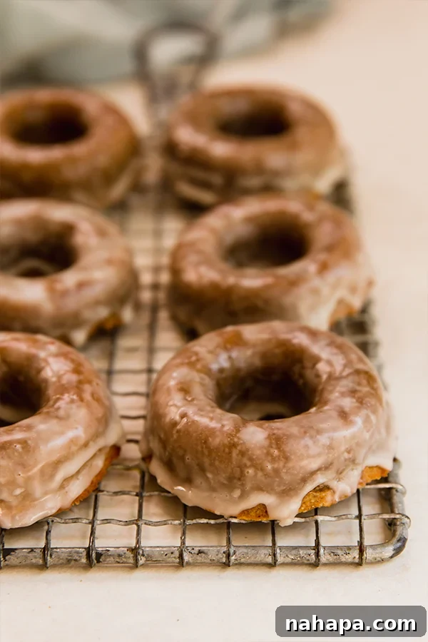 A baking sheet filled with freshly baked apple cider donuts, cooling on a rack, awaiting their delicious glaze. These healthy, grain-free treats are perfect for fall.