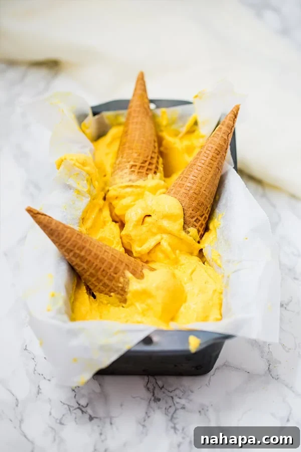 A loaf pan filled with golden mango turmeric ice cream, adorned with three crispy ice cream cones.