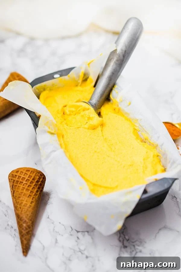 A loaf pan filled with mango turmeric ice cream, with an ice cream scoop resting within it.