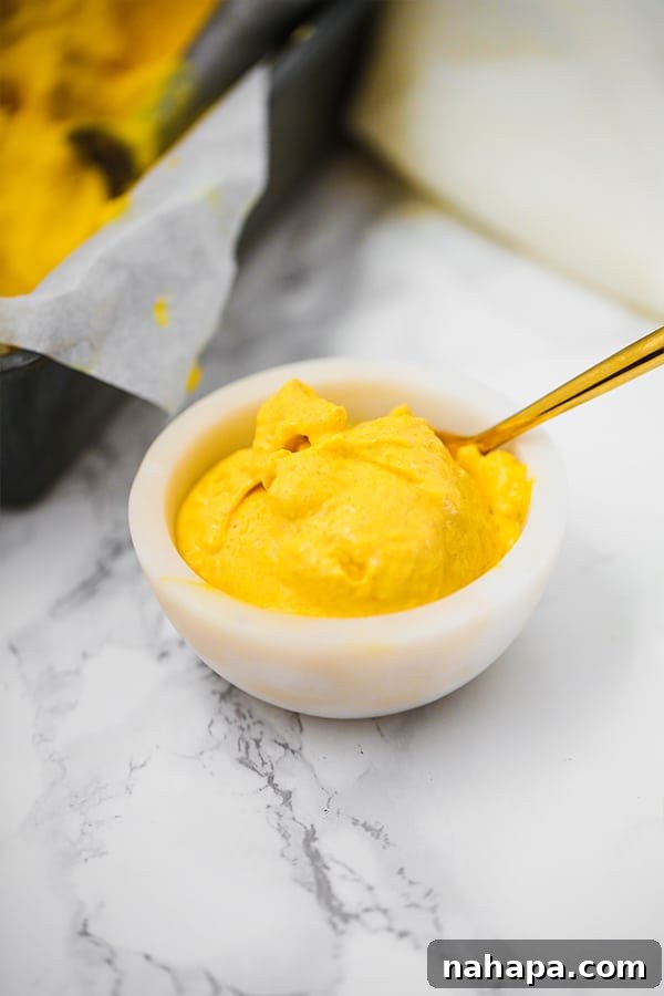 A bowl of mango turmeric ice cream with a spoon coming out of it, ready to be enjoyed.