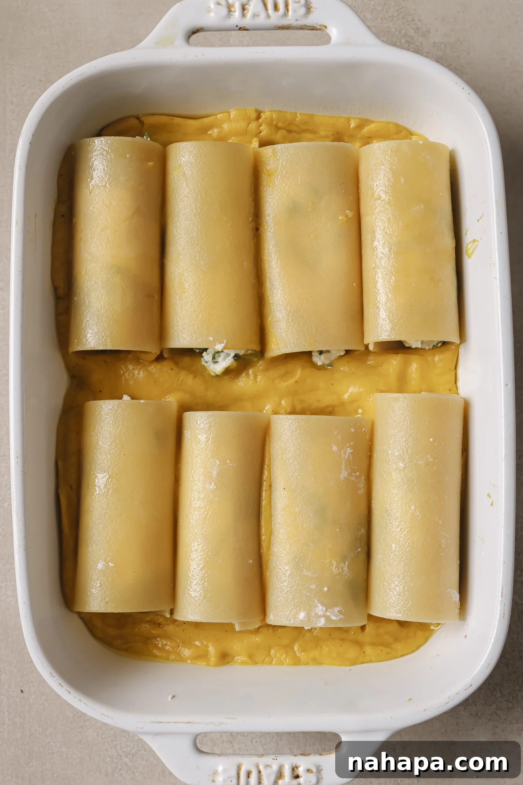 Lasagna roll ups laying in a baking dish on top of butternut squash sauce.