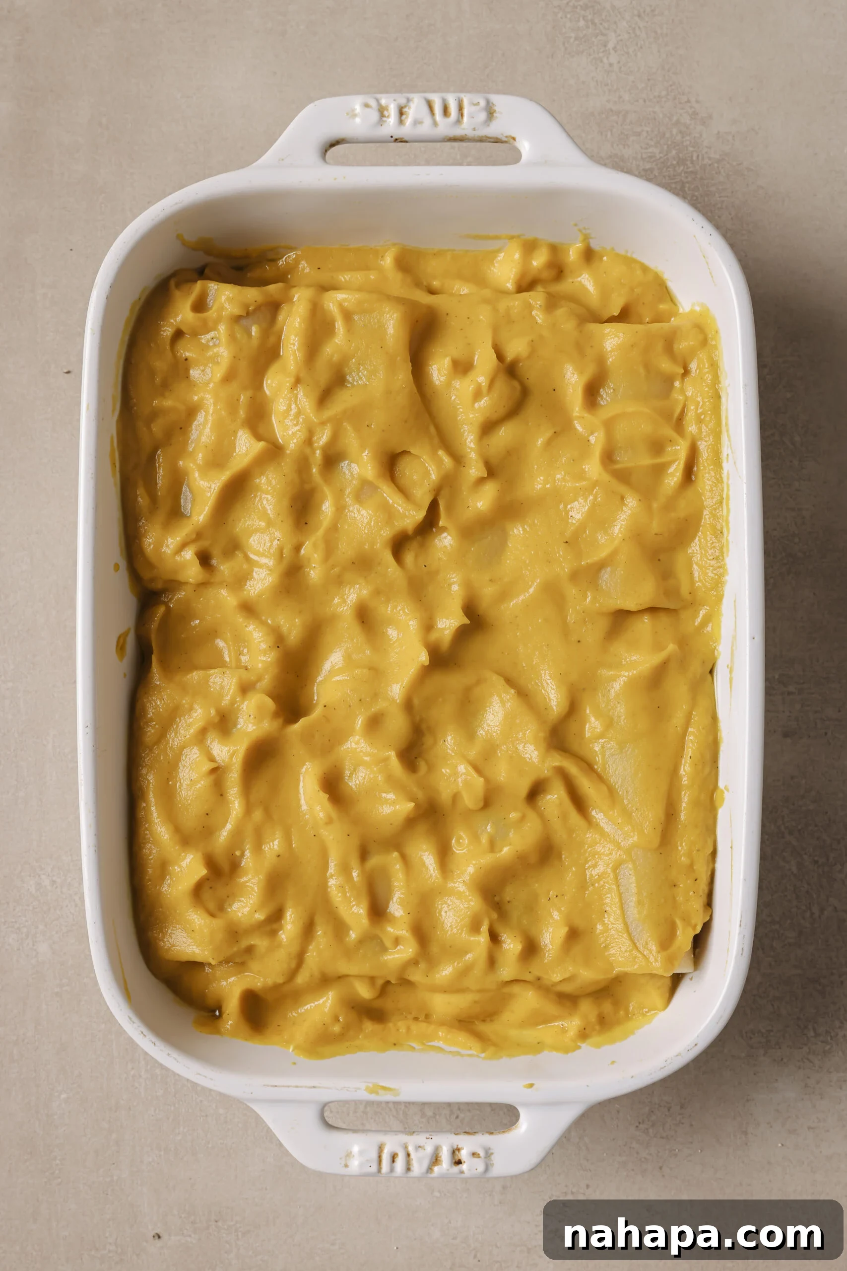 Lasagna roll ups laying in a baking dish on top of butternut squash sauce, with more sauce on top.