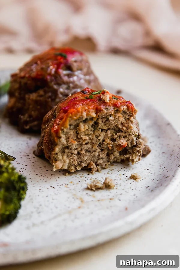 One-Pan Italian Mini Meatloaf & Roasted Vegetables (Gluten & Dairy-Free) 6 A perfectly cooked mini meatloaf on a plate, with a small bite taken out, showing its tender interior and rich sauce, surrounded by roasted vegetables.