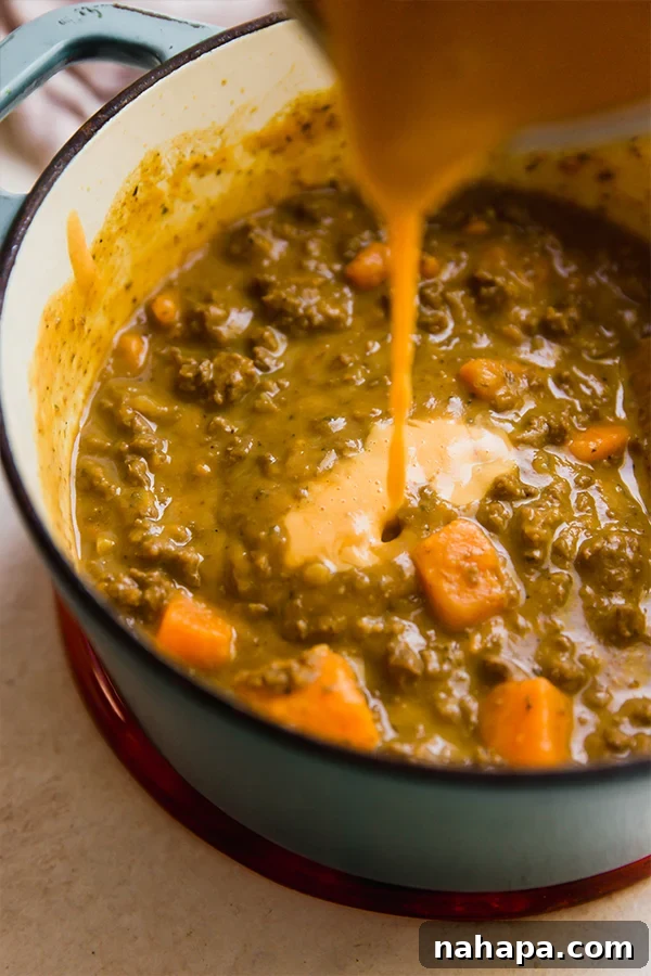A large pot filled with bubbling, rich queso chili, ready to be served, showcasing its vibrant color and hearty ingredients.