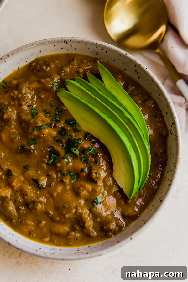 A close-up of a bowl of dairy-free queso chili, garnished with sliced avocado and fresh cilantro, highlighting its creamy texture and appealing presentation.