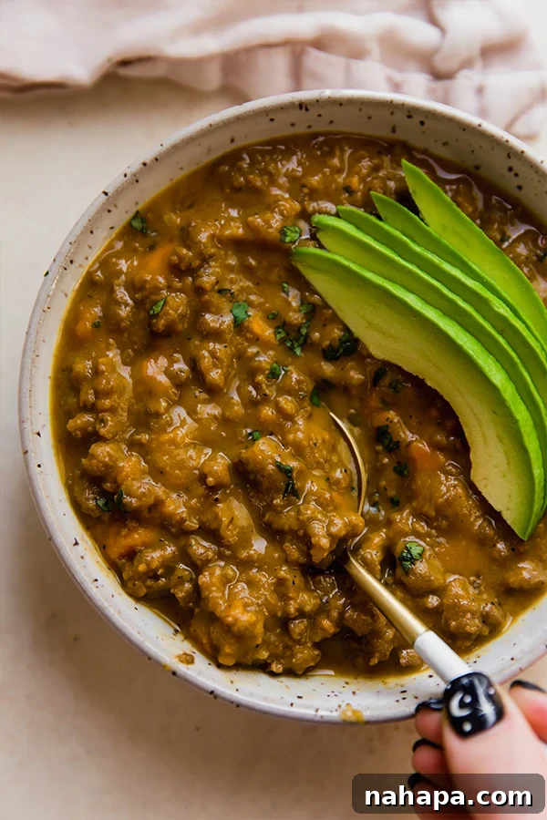 A bowl of rich, dairy-free queso chili garnished with fresh cilantro and creamy avocado slices.