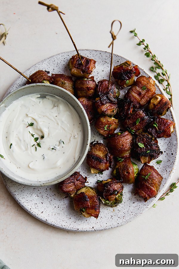 A platter beautifully arranged with bacon-wrapped Brussels sprouts and a small bowl of dipping sauce.