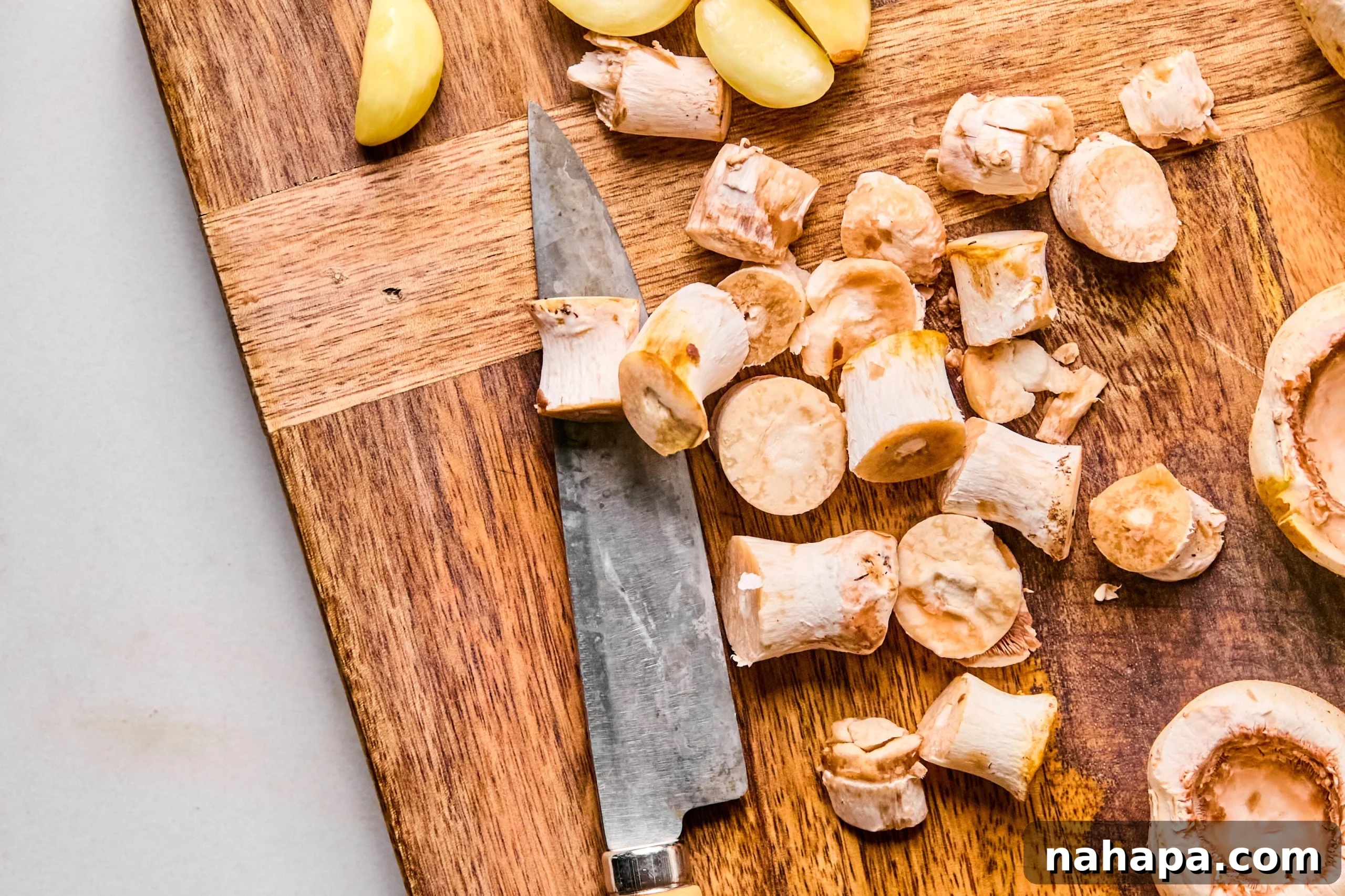 A cutting board with finely chopped garlic and mushroom stems, ready for sautéing.