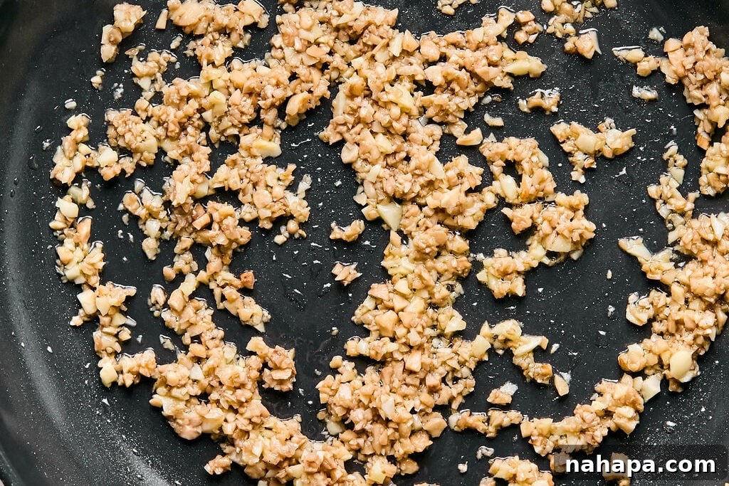 A close-up shot of garlic sautéing in a pan, its aroma beginning to fill the kitchen.