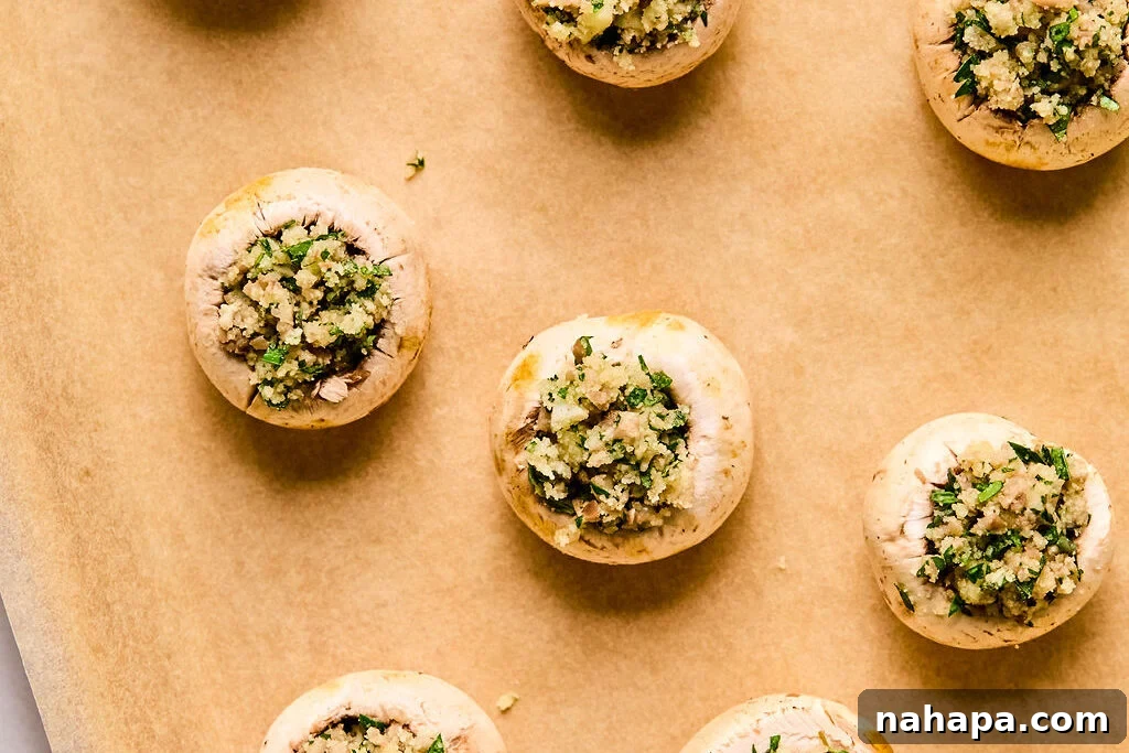 Cleaned mushroom caps generously filled with the savory mixture, glistening slightly with a drizzle of oil, awaiting their oven bake.