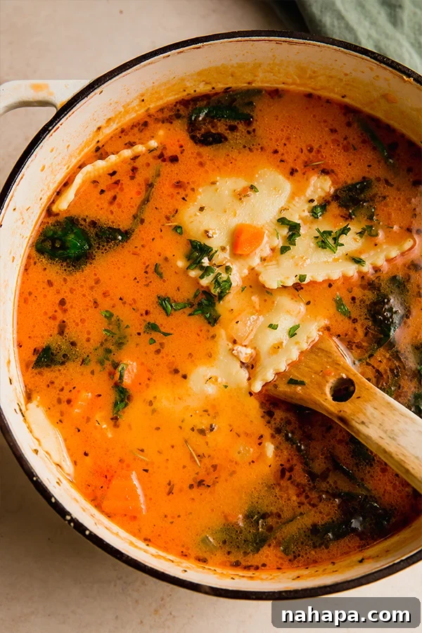 A large pot of creamy ravioli soup with a wooden spoon, ready to be served.