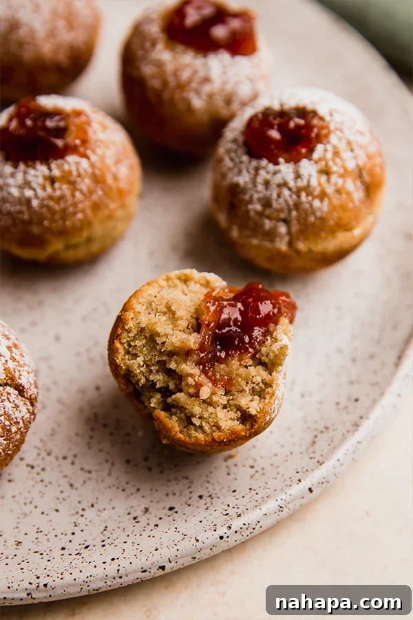 A full plate of gluten-free jelly donut holes, with a few dusted with powdered sugar, ready to be served.