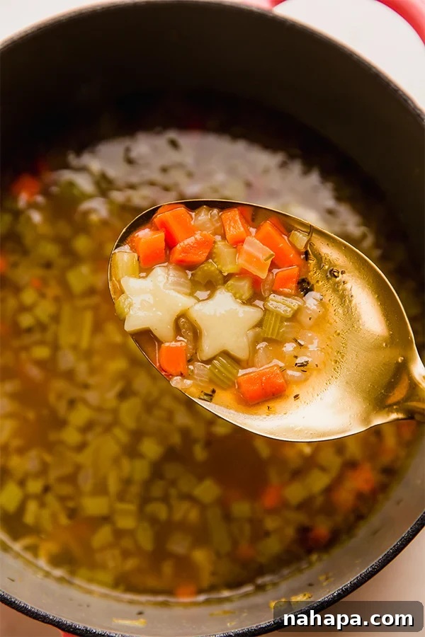 A bowl of gluten-free chicken & stars soup with a spoon, ready to eat.