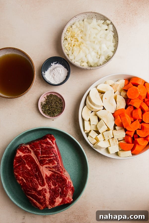 A top-down shot of all the raw ingredients for oven-baked chuck roast laid out on a wooden surface: chuck roast, various spices, garlic, onion, carrots, parsnip, sweet potato, beef broth, red wine vinegar, bay leaves, and fresh parsley.