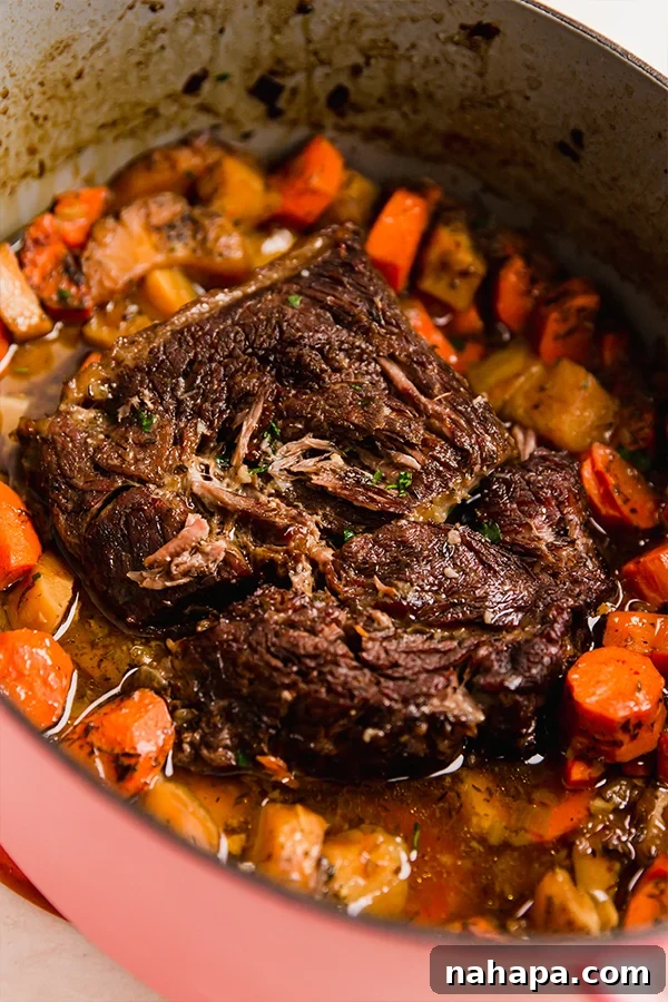A Dutch oven containing the oven-baked chuck roast, surrounded by tender vegetables and rich gravy, viewed from a slight angle.