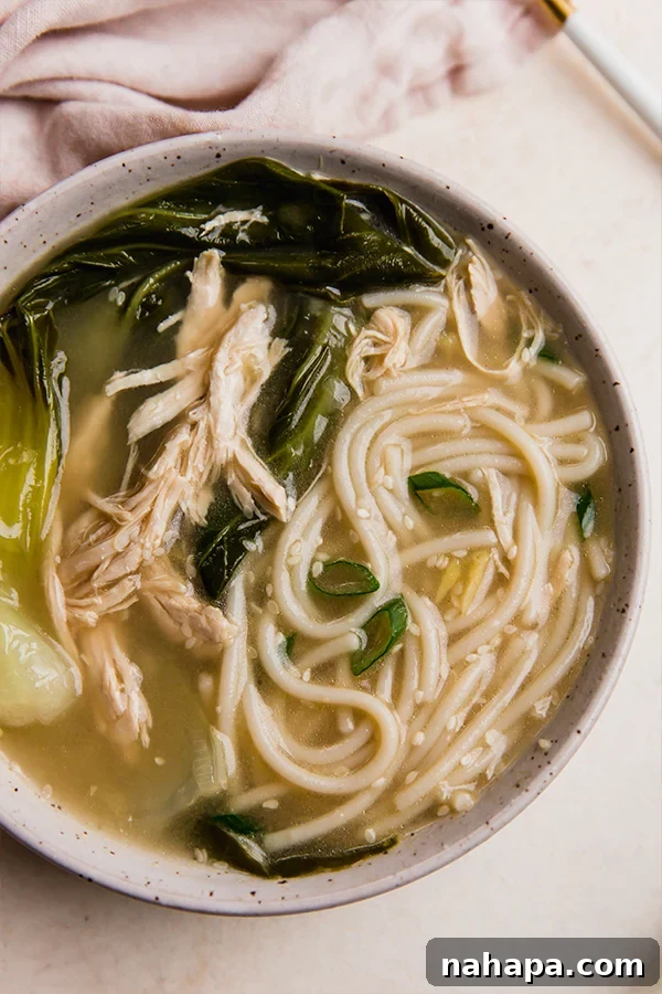 A beautifully presented bowl of bok choy noodle soup, garnished with fresh herbs.