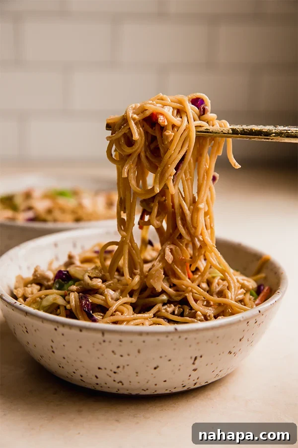 A bowl of gluten-free egg roll ramen stir fry with chopsticks picking up a mouthful of noodles and vegetables.