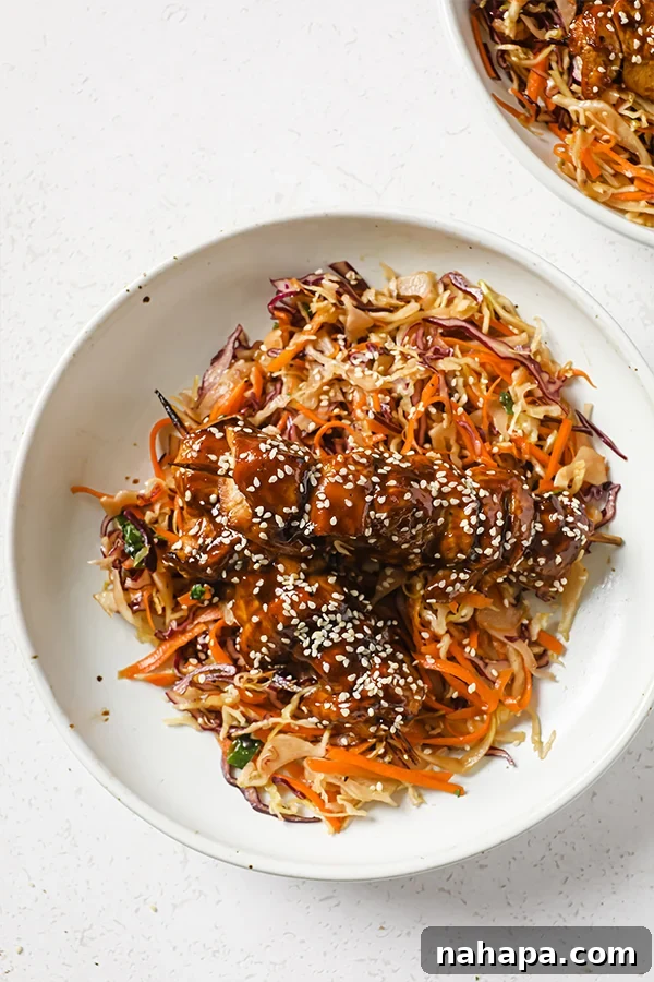 Sticky Teriyaki Chicken Skewers with Slaw 6 A beautifully arranged bowl containing Asian-inspired slaw with teriyaki chicken skewers resting on top, garnished with sesame seeds.