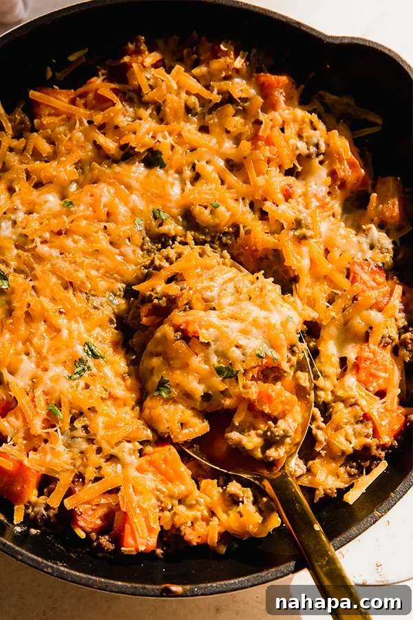 A dairy-free cheesy beef & sweet potato skillet in a cast iron pan with a serving spoon, highlighting its creamy texture.