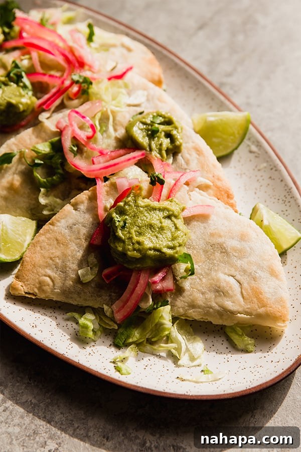 A platter of beautifully arranged baked shredded beef tacos, topped with vibrant pickled onions and creamy guacamole.