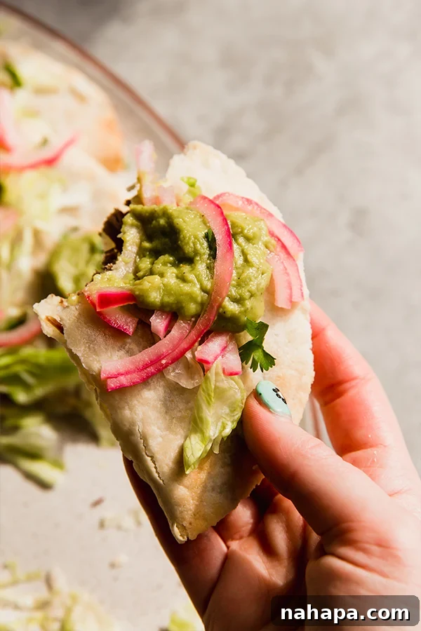 A close-up of a baked shredded beef taco held in a hand, showing its crispy texture.