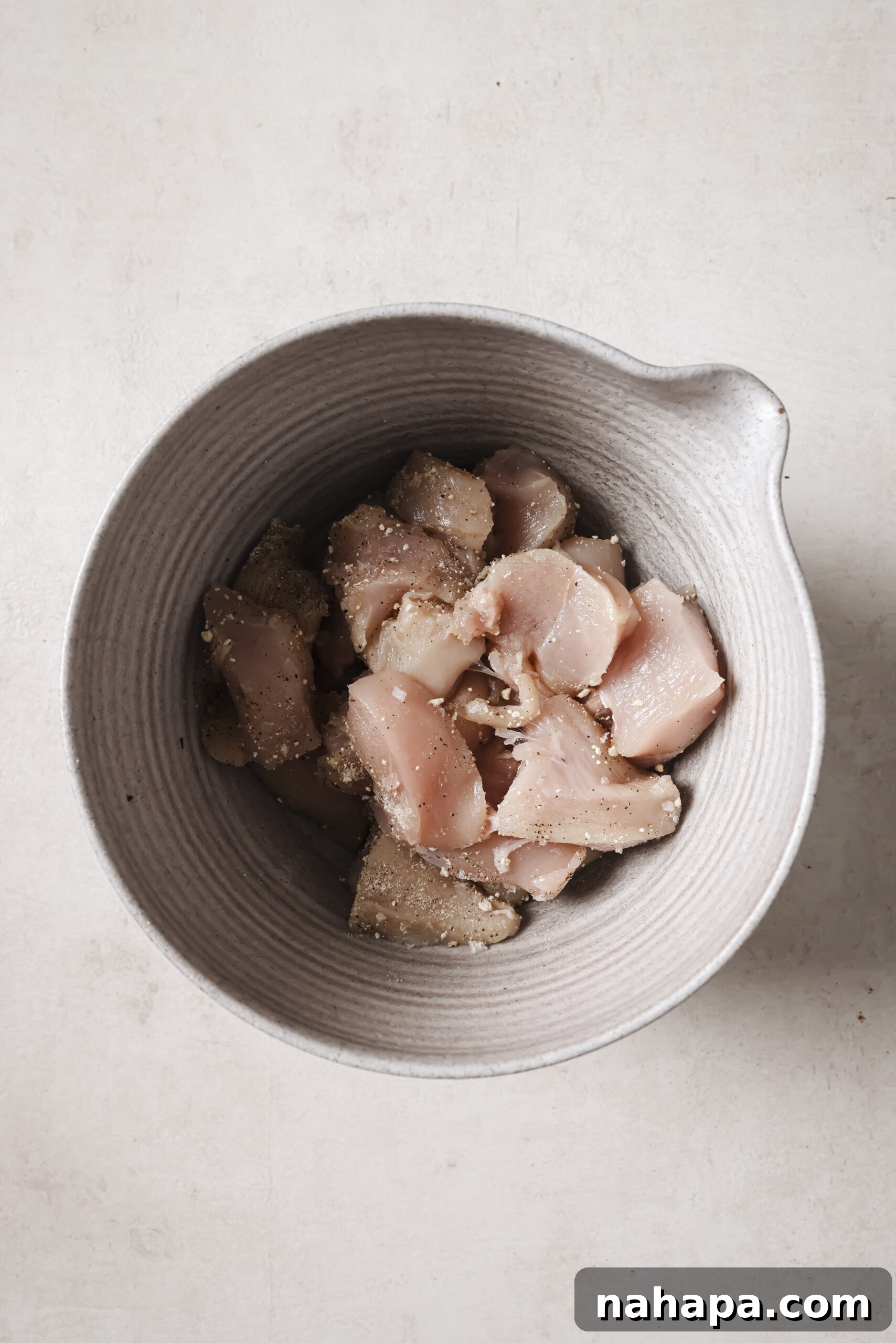 Raw cubed chicken tossed with seasonings in a bowl.