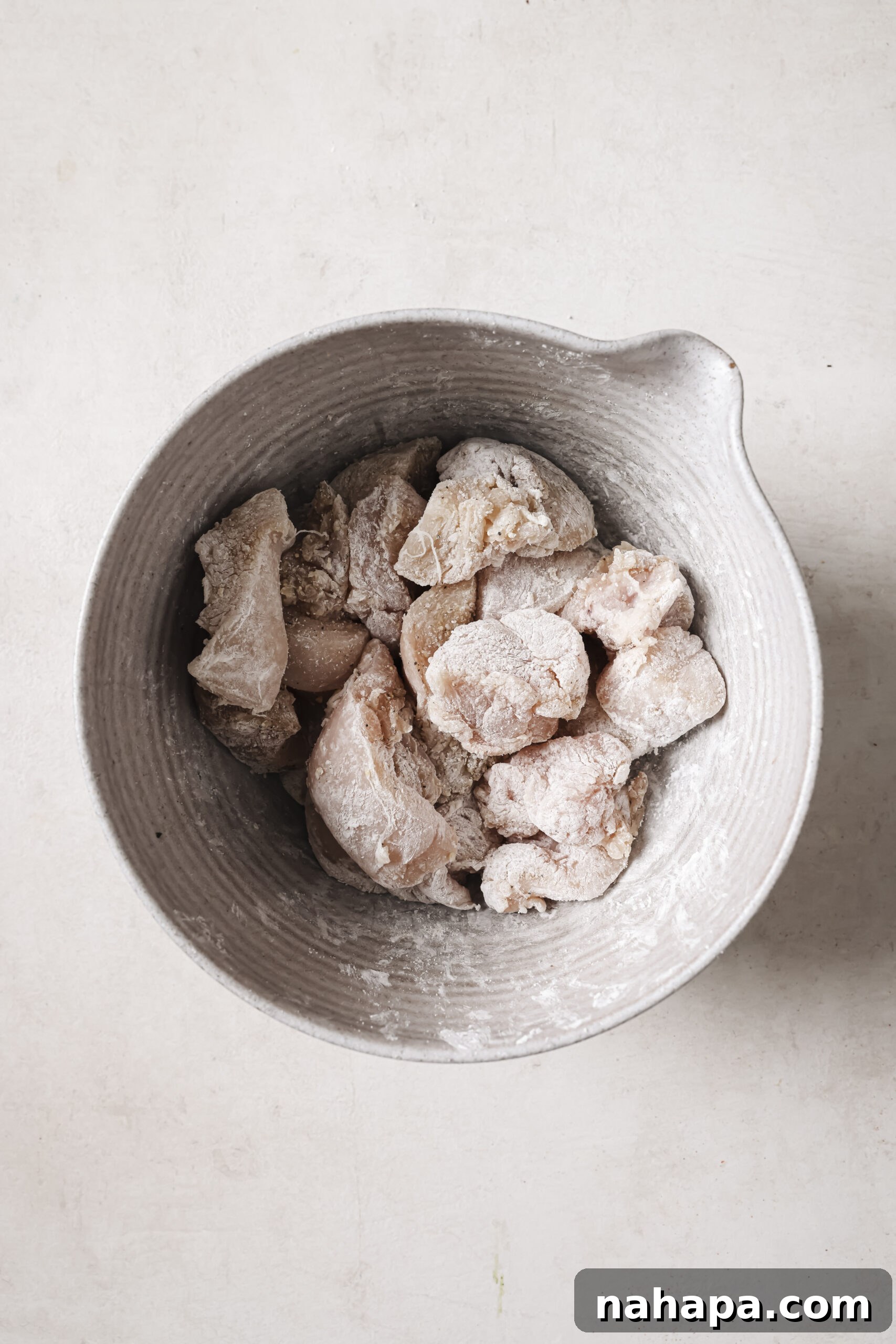 Raw cubed chicken tossed with arrowroot starch in a bowl.