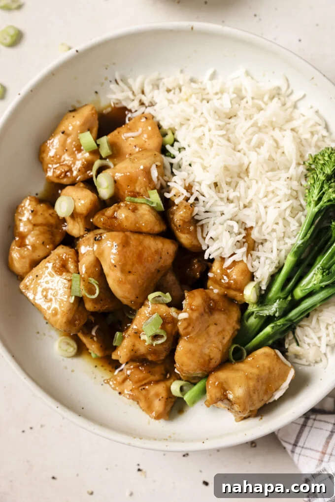 Honey butter chicken bites in a bowl topped with green onion and served with rice and broccoli.