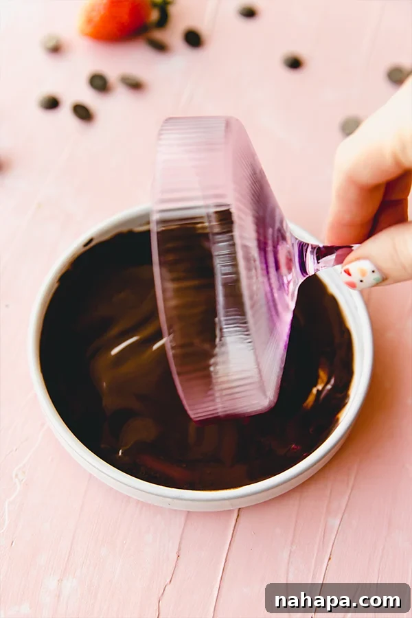 A hand expertly twirling the rim of a pink cocktail cup in melted dairy-free chocolate.