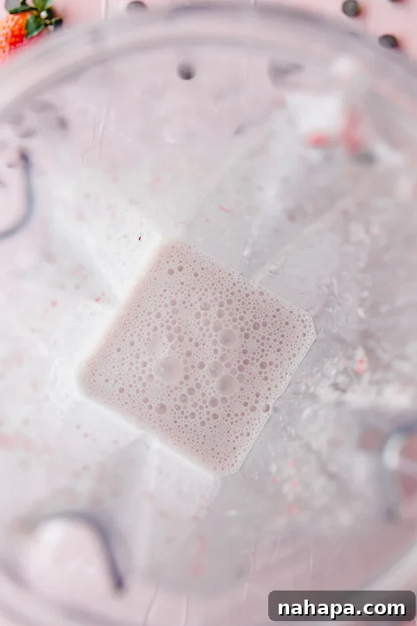 The strawberry mocktail base being blended to a smooth consistency in a blender.
