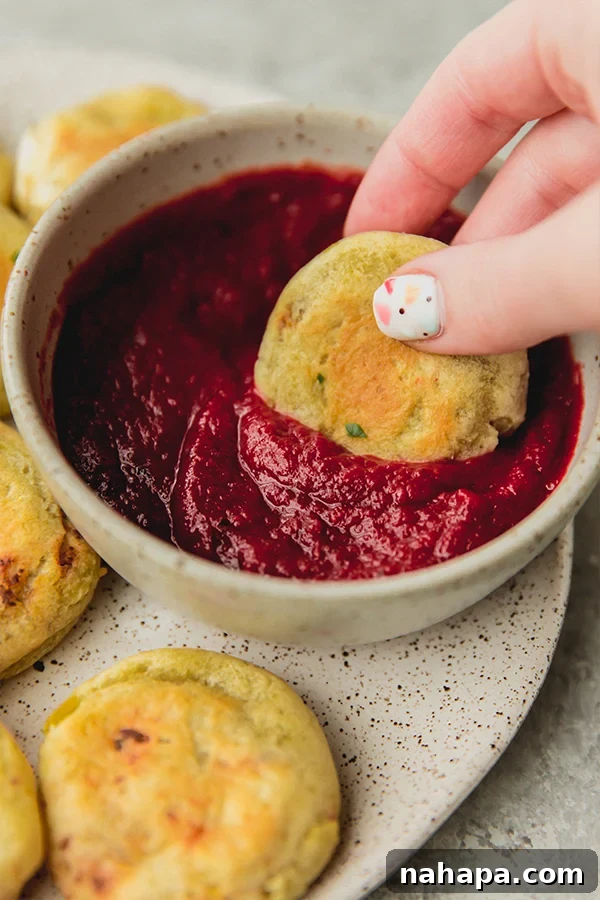Someone enthusiastically dipping a golden-brown AIP pizza roll into a bowl of vibrant nomato sauce.