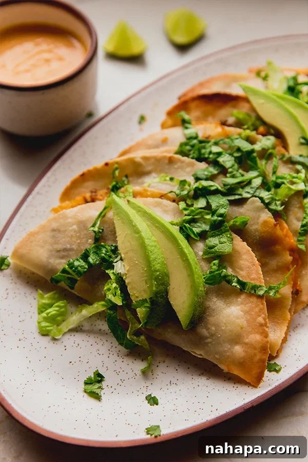 Crispy Baked Ground Beef Tacos Dairy-Free 3 A close-up view of two perfectly baked ground beef tacos, garnished with fresh avocado slices and shredded romaine lettuce, showcasing their golden-brown, crispy shells.