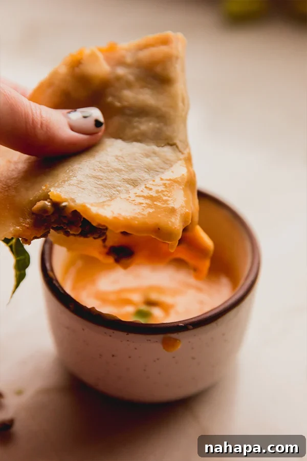 Crispy Baked Ground Beef Tacos Dairy-Free 5 A hand holds a crispy baked ground beef taco, dipping it into a bowl of creamy dairy-free cheese sauce, highlighting the perfect texture and the essential dipping experience.