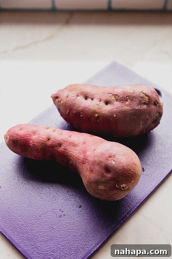 Close-up of freshly cut Japanese white sweet potatoes on a wooden cutting board, showing their purple skin and white flesh.