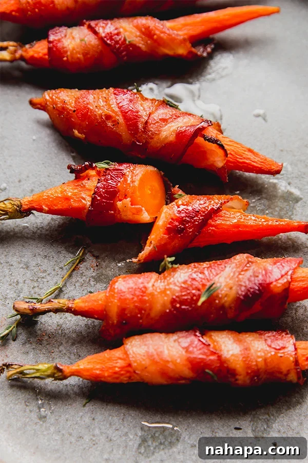 A few bacon-wrapped carrots on a plate with one cut open, revealing the tender cooked carrot inside.