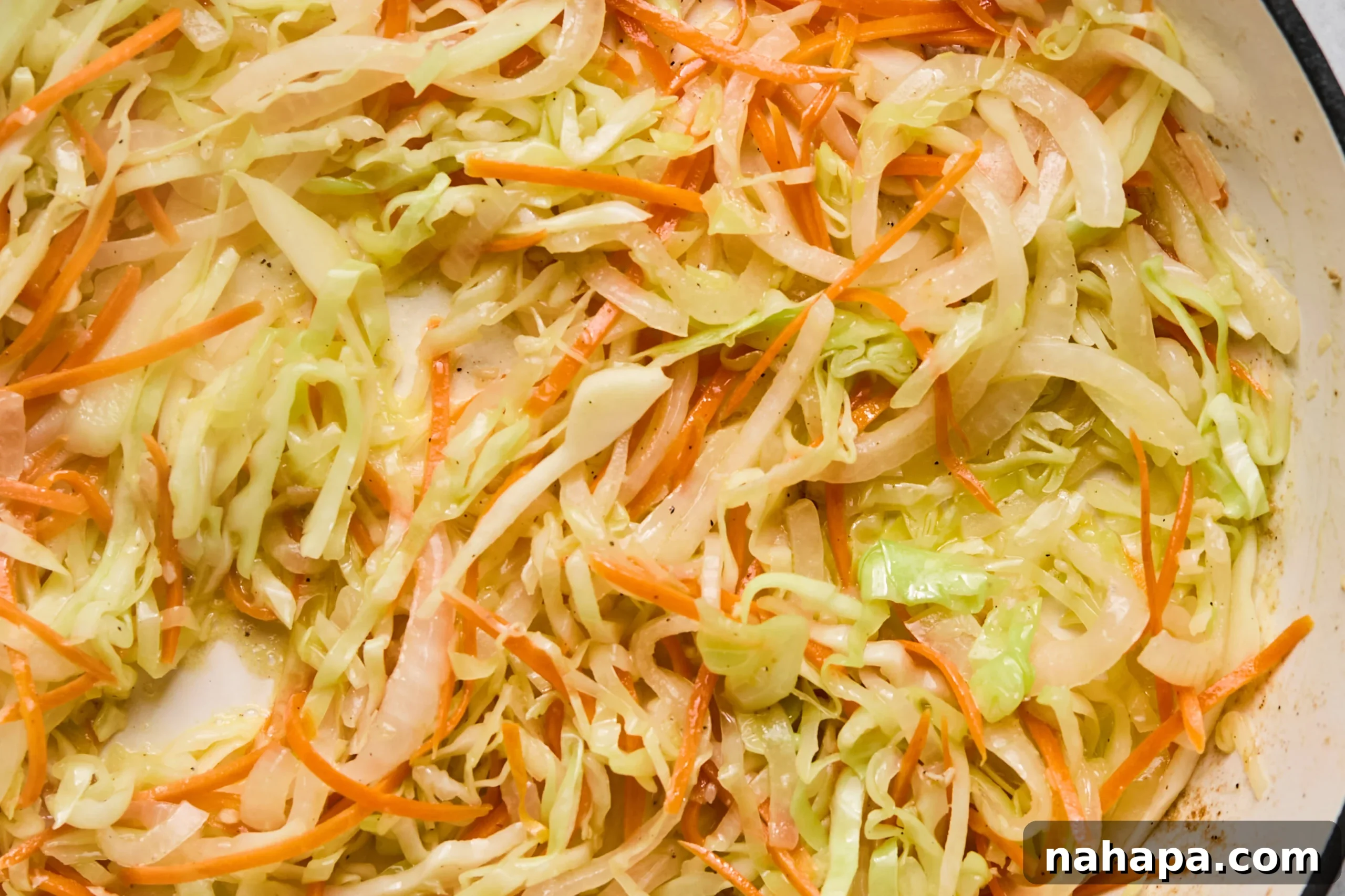 Pad Woon Sen Flavorful Gluten Free Glass Noodle Stir Fry 7 A vibrant mix of shredded cabbage, sliced onion, and shredded carrots sautéing in a pan, showcasing their softening texture and bright colors.