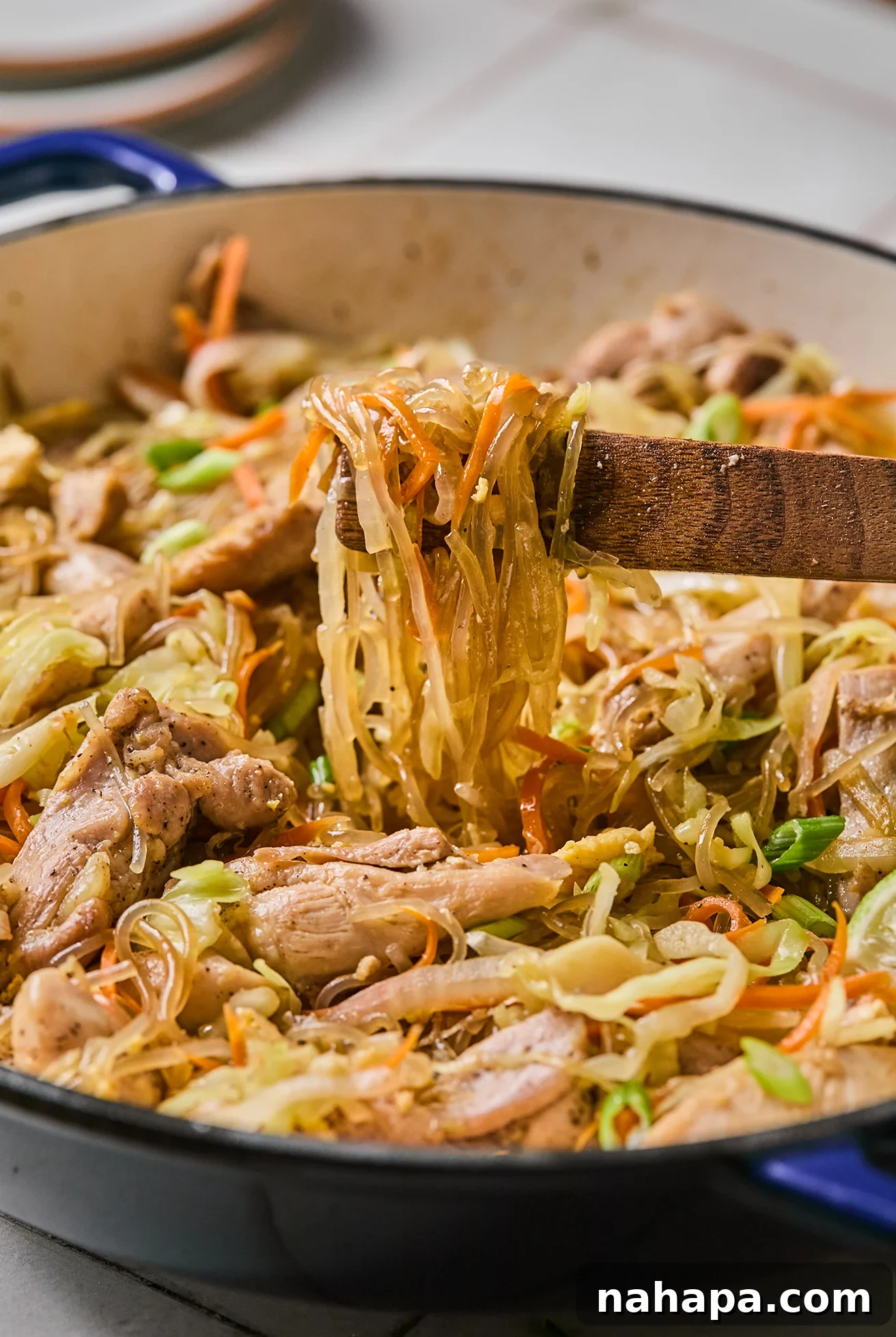 Pad Woon Sen Flavorful Gluten Free Glass Noodle Stir Fry 10 A close-up view of Pad Woon Sen in a large pan, showing the glossy glass noodles mixed with chicken and vegetables, being tossed with tongs.