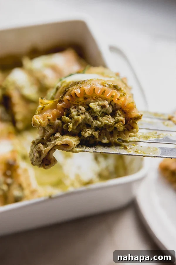 Gluten-Free White Pesto Lasagna Roll-Ups 6 A serving spatula lifting a single white pesto lasagna roll-up from a casserole dish, ready to be plated.