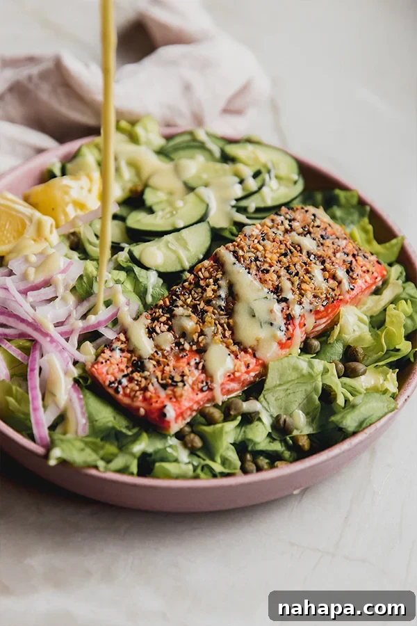 Everything Bagel Salmon Delight 2 A bowl of the everything bagel salmon salad with creamy dressing being generously poured on top, highlighting its freshness and vibrant colors.
