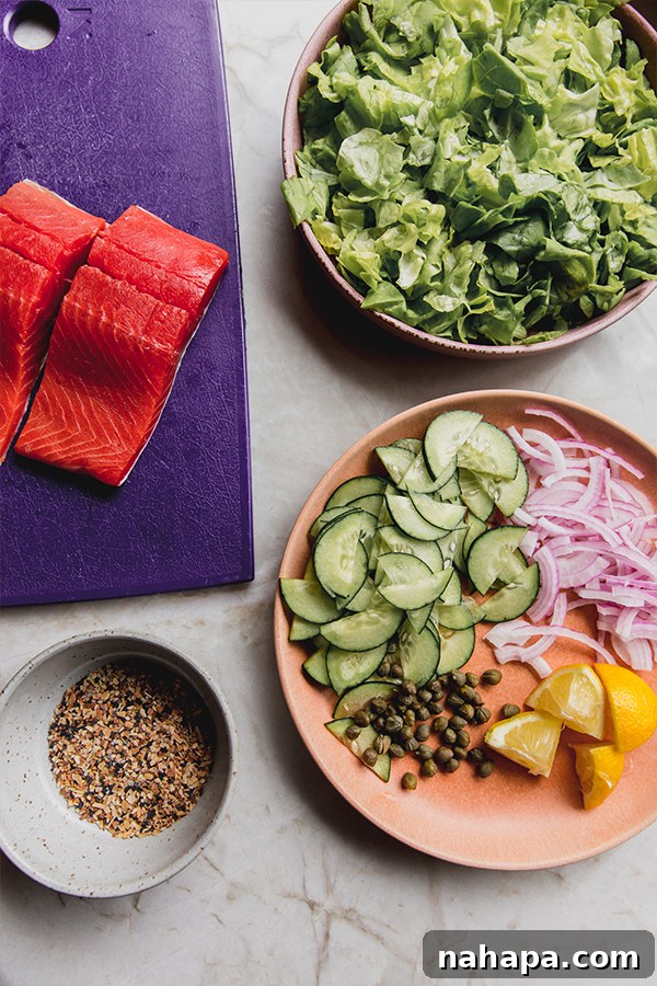 Everything Bagel Salmon Delight 3 All the fresh ingredients for making the everything bagel salmon salad laid out on a clean surface, including salmon, lettuce, cucumber, red onion, capers, and dressing components.