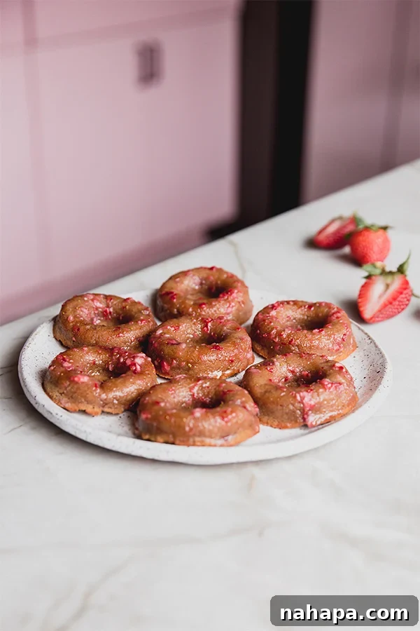 A pristine plate filled with perfectly glazed gluten-free strawberry mini donuts, garnished with fresh strawberry slices, sitting invitingly on a kitchen counter.