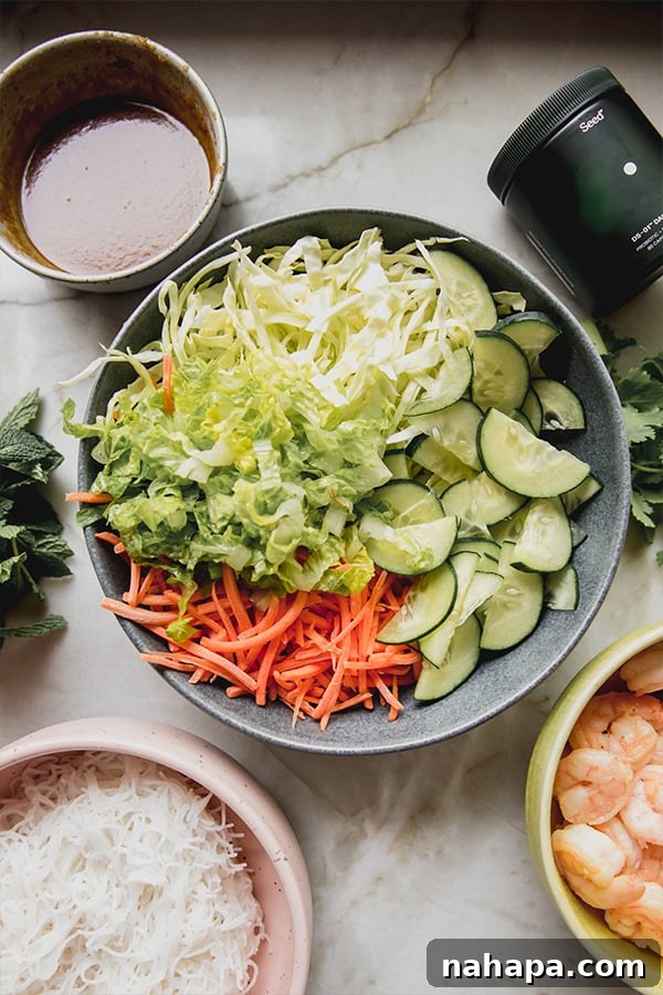 Close-up of fresh ingredients for spring roll bowls, including shredded cabbage, carrots, shrimp, and herbs