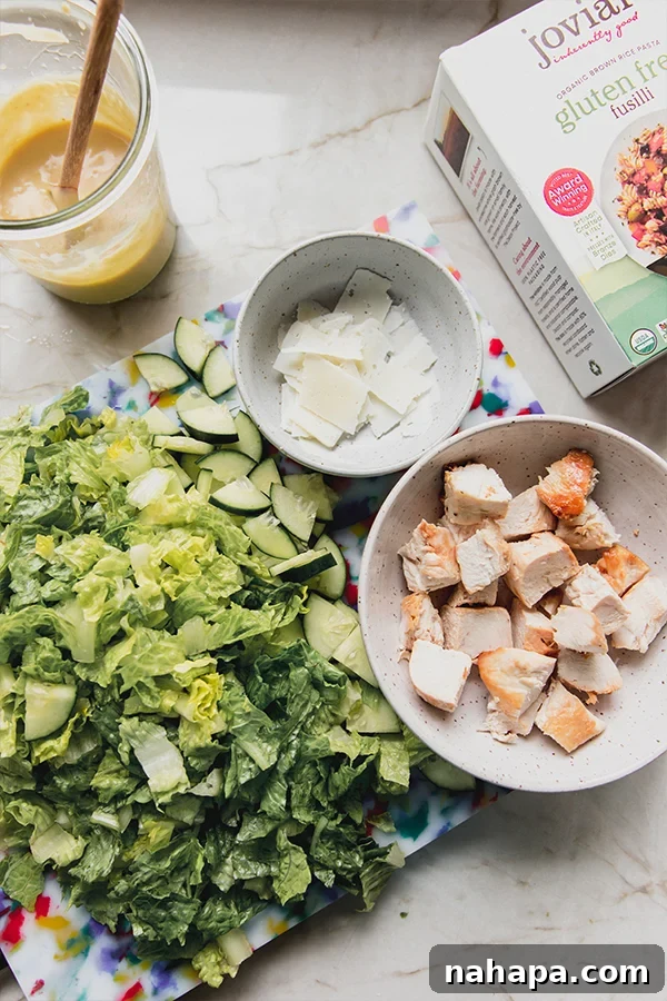 The vibrant ingredients for chicken caesar pasta salad laid out on a kitchen countertop.