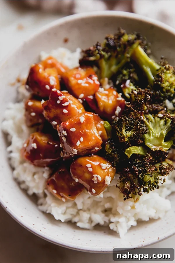A bowl of sheet pan sesame chicken in a bowl ready to be eaten. Garnished with sesame seeds.